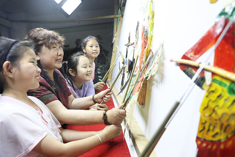 皮影藝人指導(dǎo)小朋友表演皮影戲。